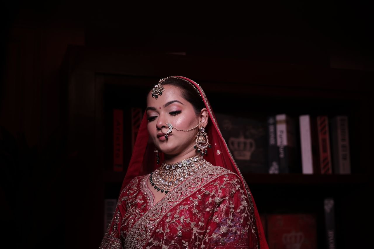 Elegant Indian bride in red sari with intricate jewelry, posing indoors.